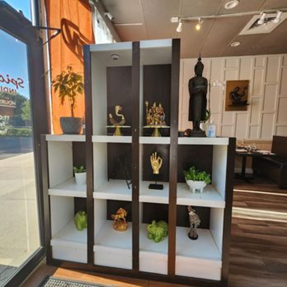 A decorative shelf with Indian artifacts and plants, next to a window and dining area.