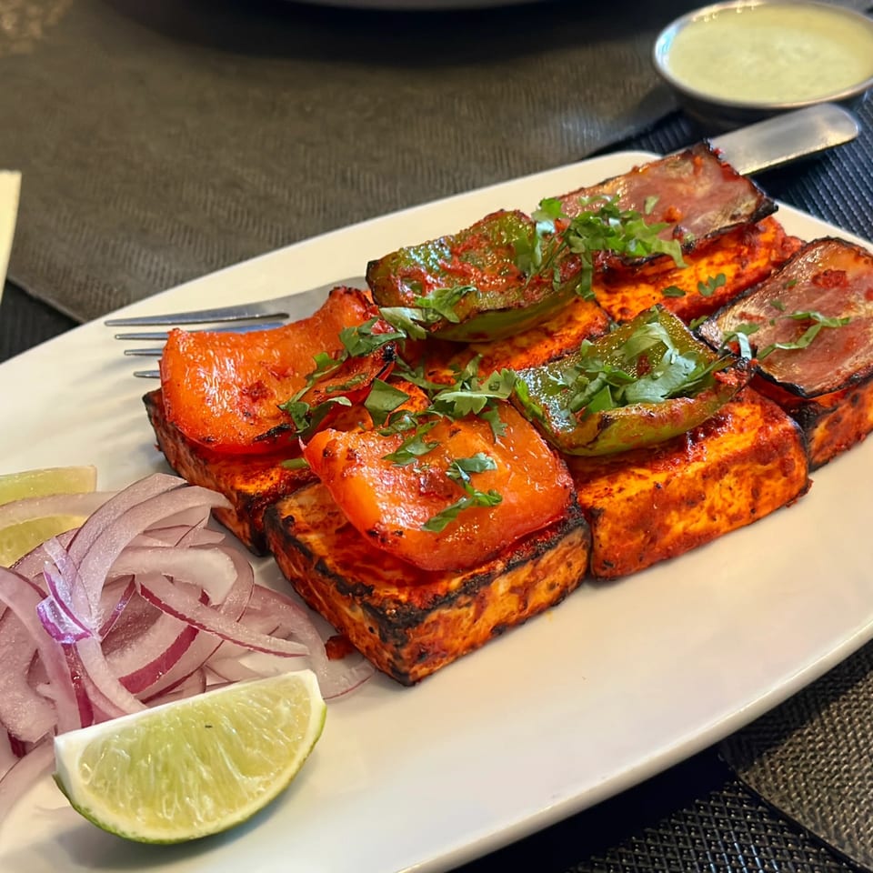 Grilled paneer tikka with bell peppers, cilantro, red onions, and lime on a white plate.