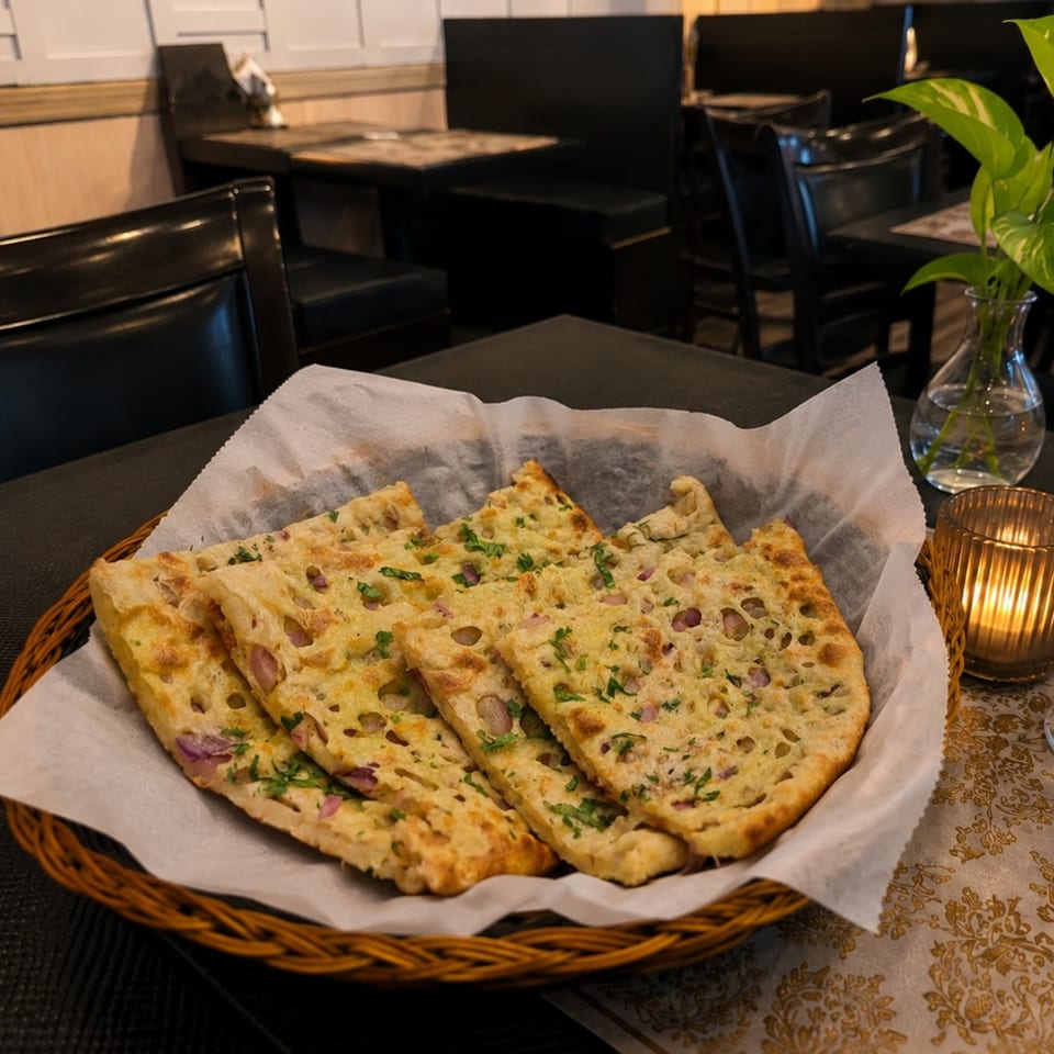 Basket of naan bread with herbs and onions on a table in a restaurant setting.