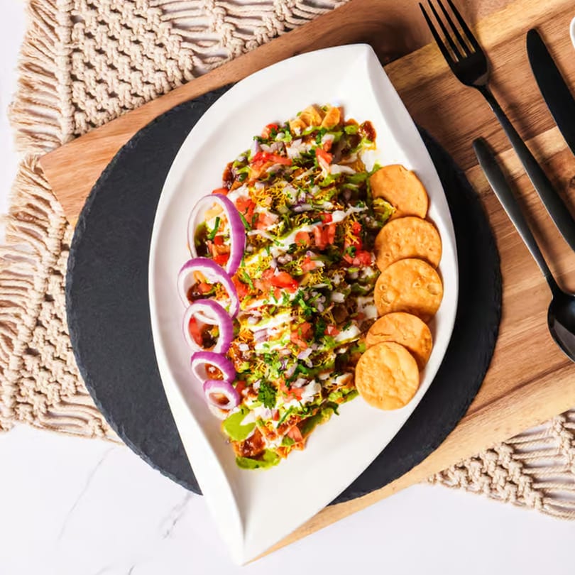 Indian chaat with red onions, tomatoes, and crispy flatbread on a white plate.