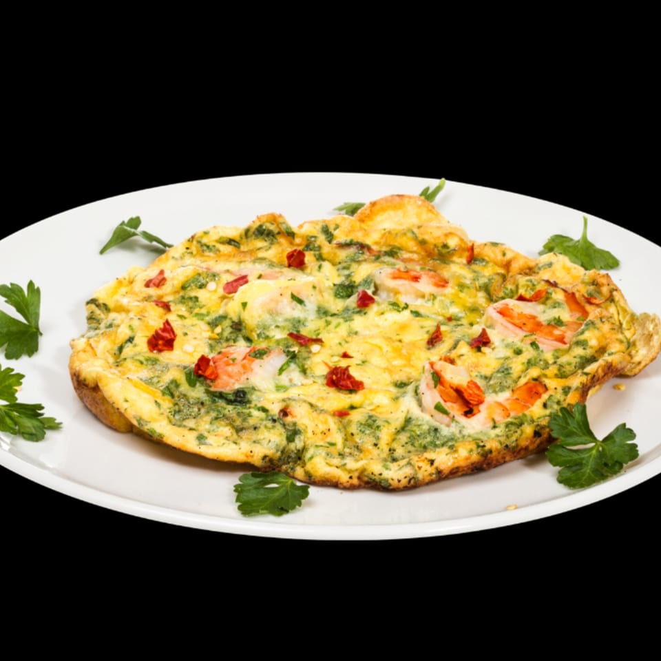 A golden omelet with shrimp, green herbs, and red chili flakes on a white plate.