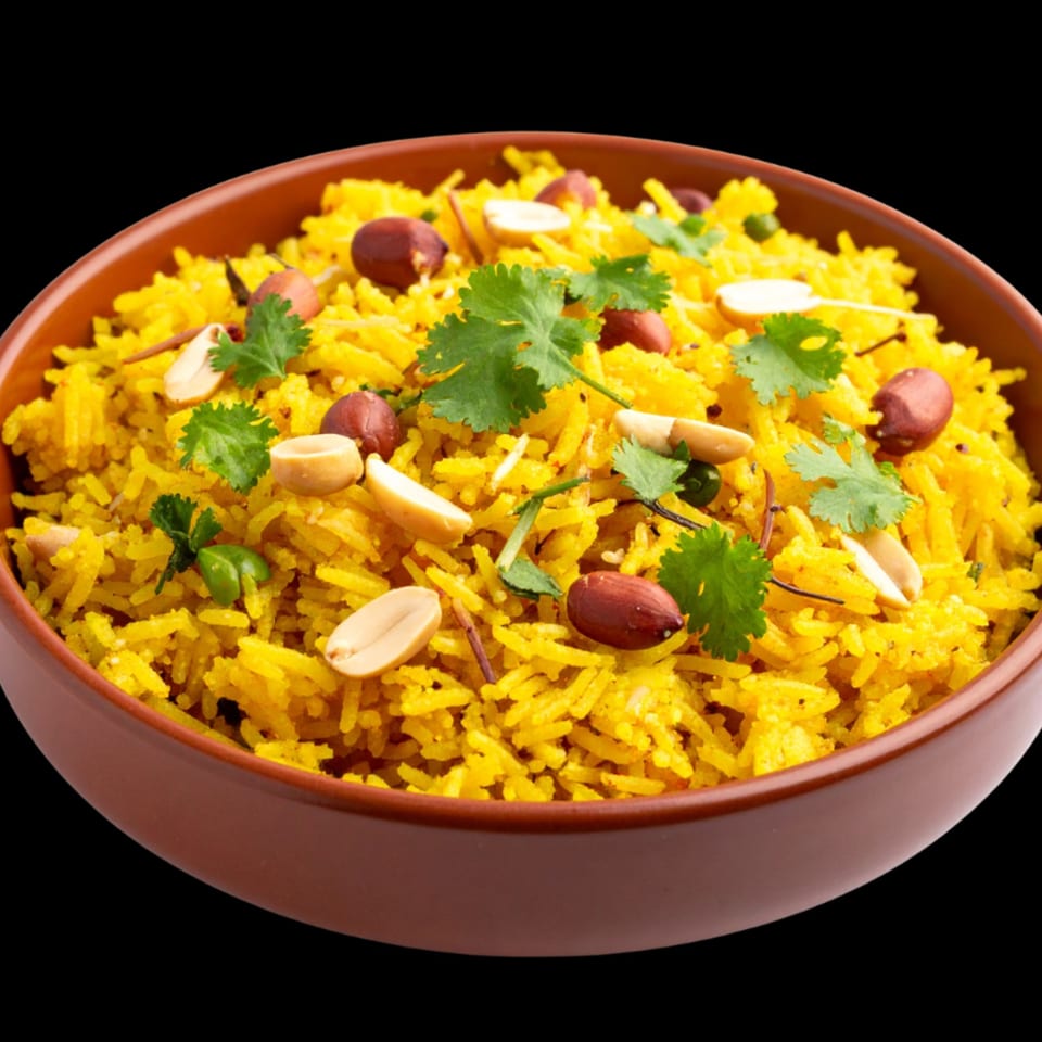 Close-up of a brown bowl filled with yellow rice, garnished with peanuts and fresh cilantro.
