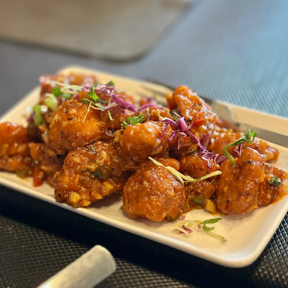 Close-up of crispy orange chicken pieces garnished with red cabbage and green herbs on a white plate.