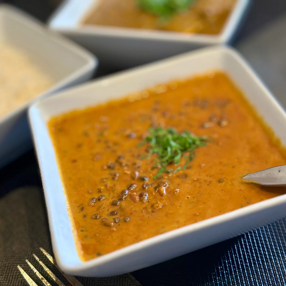 Close-up of a square white bowl filled with orange curry, garnished with green herbs.