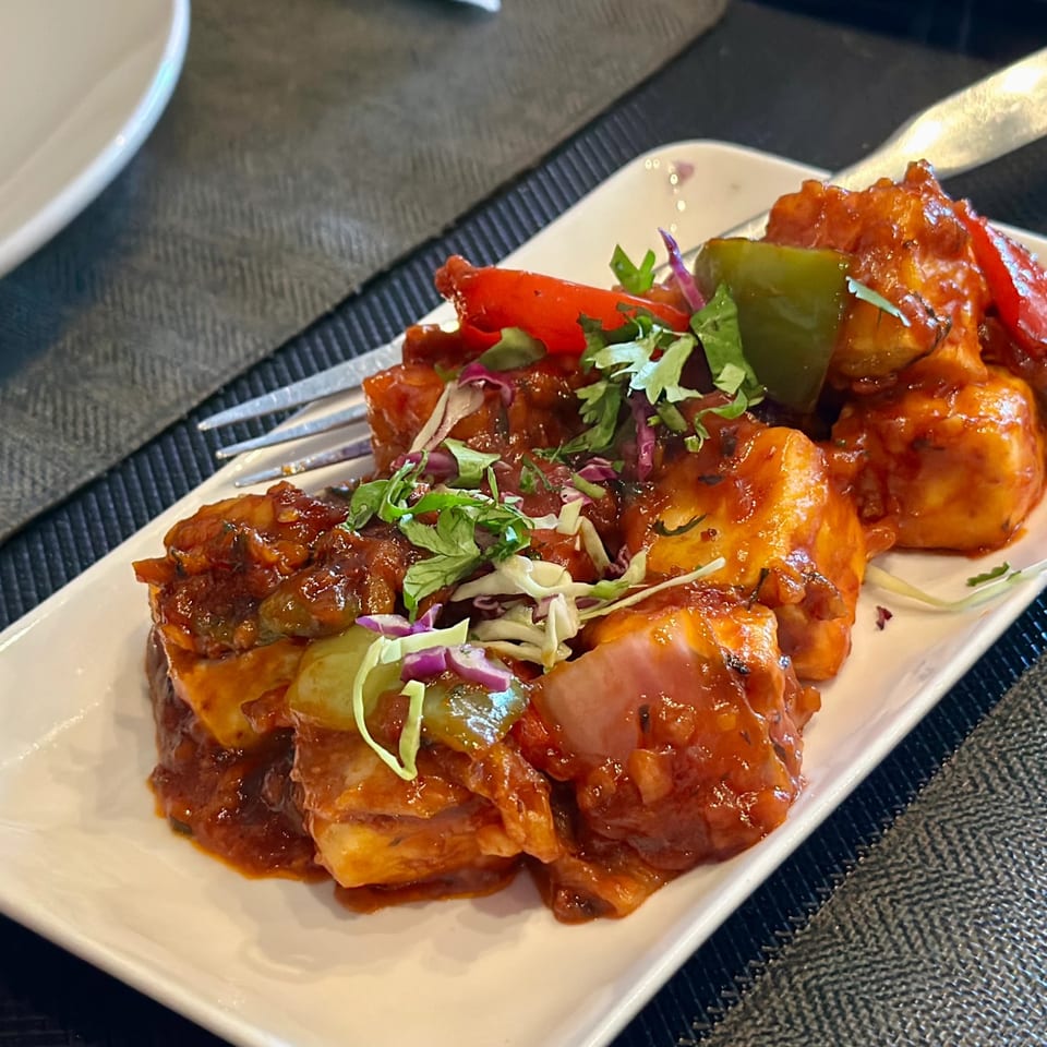 Spicy paneer chili with bell peppers, onions, and herbs on a white rectangular plate.