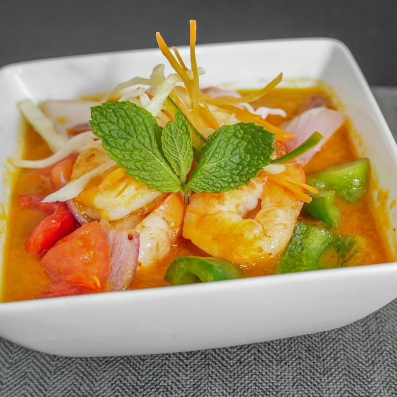 Indian shrimp curry with bell peppers, tomatoes, onions, and mint in a white bowl.