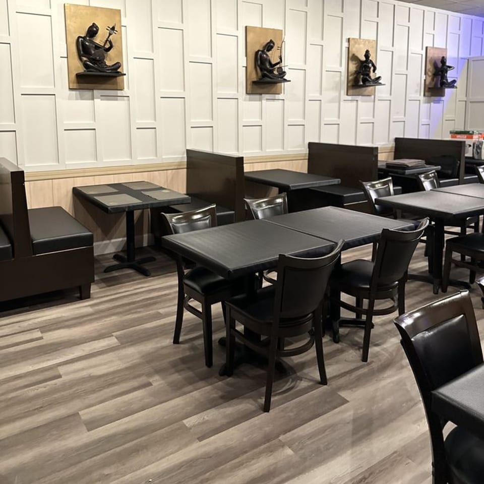 Interior of Spice Grill Indian Cuisine with dark tables, chairs, booths, and wall art.