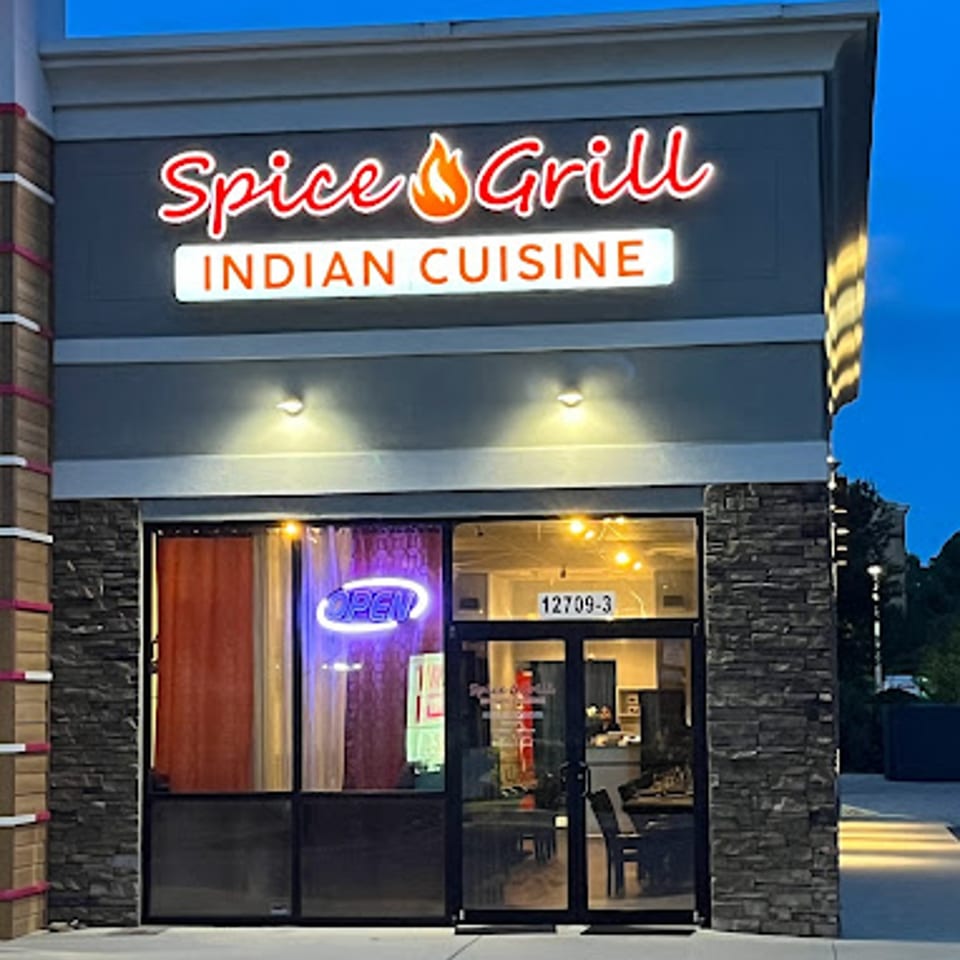 Exterior of Spice Grill Indian Cuisine at dusk, with a glowing red sign and an "OPEN" neon sign.
