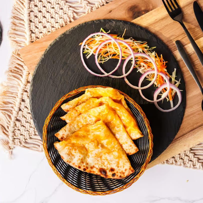 Indian naan bread in a basket with a side of sliced onions and shredded carrots.