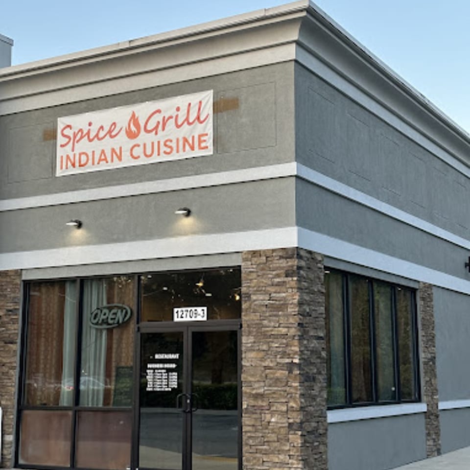 Exterior of Spice Grill Indian Cuisine restaurant with a gray facade, stone accents, and large windows.