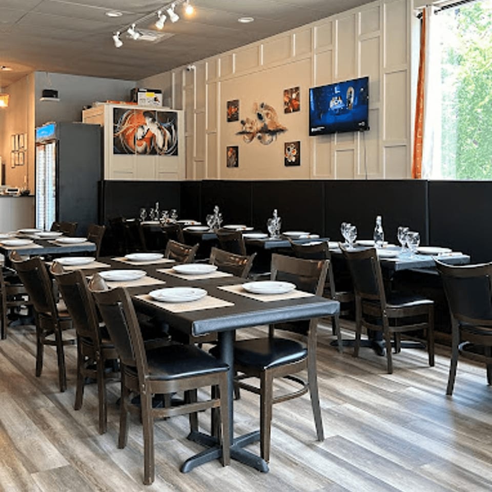 Interior of Spice Grill Indian Cuisine, featuring set tables, dark chairs, and decorative wall art.